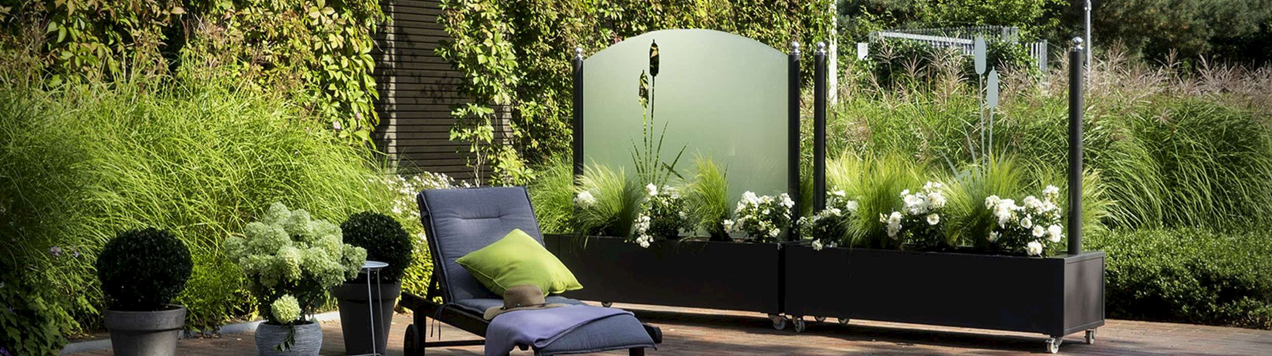 Terrasse mit Windschutz aus Glas, Pflanzen und einer Liege